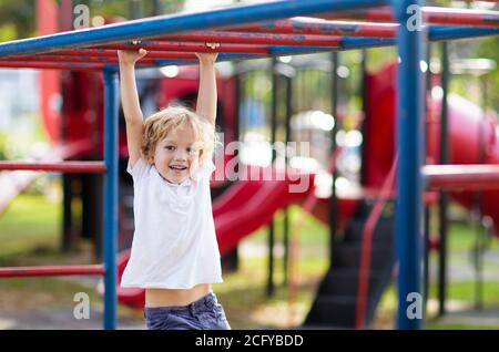 Kinder spielen auf dem Spielplatz im Freien bei Regen. Kinder spielen auf dem Schul- oder Kindergartenhof. Aktives Kind auf bunten Affenstäben. Gesunde Sommeraktivität für Stockfoto