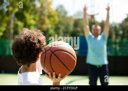 Rückansicht des sportlich lockigen Jungen, der Korbball wirft Stockfoto