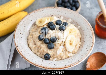 Haferflocken mit Heidelbeeren, Banane und Kokosflocken. Gesundes Frühstück Porridge Schüssel Stockfoto