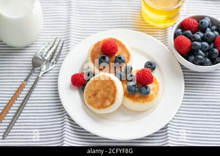 Quark-Fritten mit Sommerbeeren und Honig auf weißem Porzellanteller serviert. Gesundes, süßes Frühstück Stockfoto