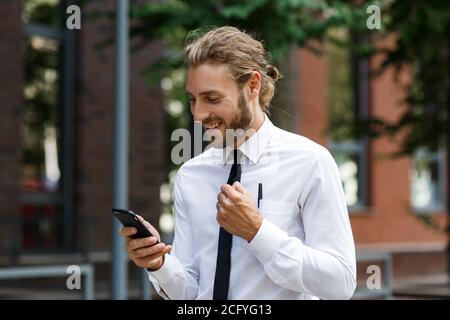 Aufgeregt und glücklich Geschäftsmann Gewinner hält ein Smartphone in Euphorie vom Sieg.Porträt eines lockigen jungen Geschäftsmann Manager in Ein Weiß Stockfoto