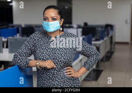Porträt der erfolgreichen indischen Geschäftsfrau trägt Covid Schutzmaske und steht vor Bürohintergrund, Corporate Umwelt. Stockfoto