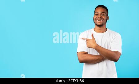 African Guy Zeigt Finger Beiseite Auf Copyspace, Blauer Hintergrund, Panorama Stockfoto