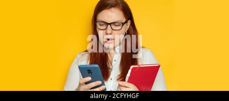 Wütend Geschäftsfrau in blauem Hemd und Brille verwendet ein Smartphone Und hält einen roten Notizblock in den Händen Büro Stockfoto