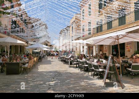 ALCUDIA, SPANIEN - 10. AUGUST 2019: Restauranttische auf der Straße in der Altstadt von Alcudia, Mallorca, Spanien. Stockfoto