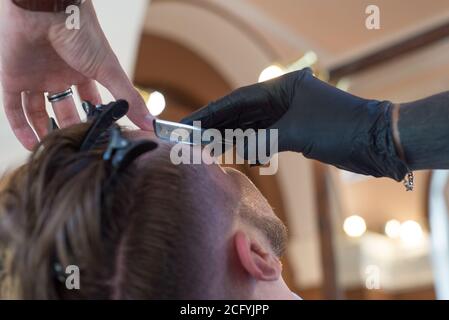 Barber Rasieren ein junger bärtiger Barbier Shop Kunde Kerl mit einem Rasiermesser. Nahaufnahme. Barthaare, gefährliche Rasiermesser, professionelle Haare und Bartpflege. Mann Stockfoto