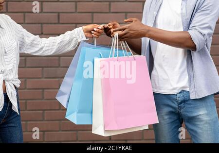 Ausgezeichnete Rabatte und viele Kauf. afroamerikanischer Mann, der der Frau Papiertüten übergab Stockfoto