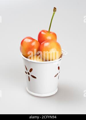 Beeren aus gelber Süßkirsche in einem weißen Metalleimer auf weißem Hintergrund. Stockfoto