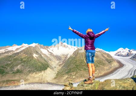 Wandern in den Schweizer Alpen, Kanton Wallis, Europa. Blonde unbeschwerte Frau mit spektakulärem Blick auf den Aletschgletscher von Eggishorn aus Stockfoto