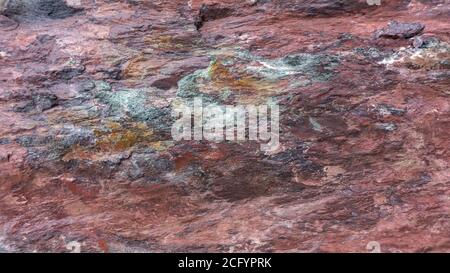 Hintergrund aus rotem Jaspis mit hellen Spritzern von lila, türkis und orange Mineral. Steintextur aus Gabbro-Diabase. Felsbrocken aus rotem Jaspis in Stockfoto