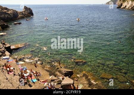 Menschen, die am felsigen Ufer sonnenbaden und im Meer an der Bucht von Lord Byron im alten Fischerdorf Porto Venere, La Spezia, Italien schwimmen Stockfoto