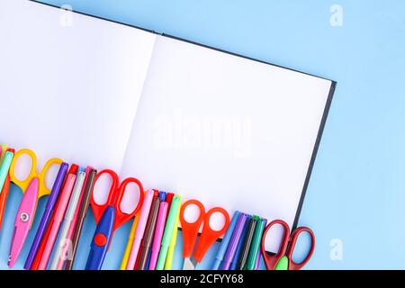 Schulbedarf. Zurück zur Schule Designelemente. Bunte Marker und Schere auf geöffnetem leeren Notizblock auf hellblauem Papierhintergrund. Stockfoto