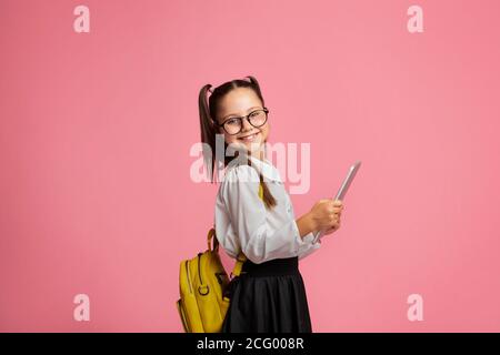 Untergeordnetes Element, das Gadgets zum Lernen verwendet. Fröhliche Schulmädchen in Brille mit Rucksack hält digitale Tablette Stockfoto