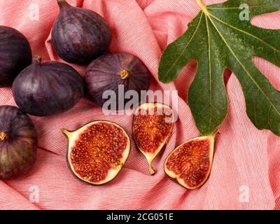 Ganz, halb, Viertel frische reife Feigenfrüchte und Feigenbaumblatt auf einem pastellroten Tuch. Süße Früchte und Beeren. Vegetarische, Rohkost Ernährung. Stockfoto