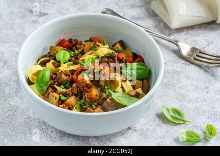 Linsen- und Auberginenragu mit Tagliatelle-Pasta und frischem Basilikum - gesundes vegetarisches Essen Stockfoto