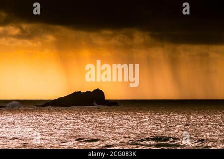 Regenwolken und ein spektakulärer feuriger Sonnenuntergang über Goose Island bei Fistral in Newquay in Cornwall. Stockfoto