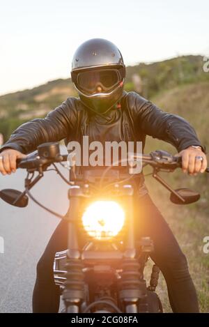 Biker im Helm sitzen und entspannen auf Oldtimer-Motorrad bei Sonnenuntergang. Stockfoto