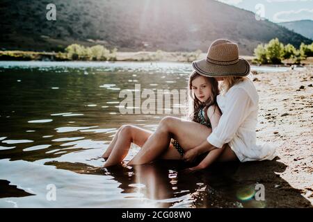 Mutter und Tochter sitzen ruhig im Wasser auf einem Seeufer Stockfoto