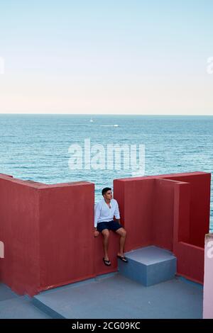 Junger lateinischer Mann meditativ in einem roten Gebäude, Meer im Hintergrund Stockfoto