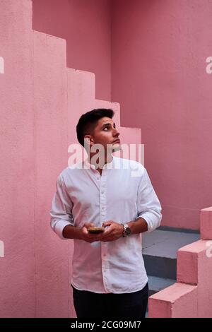 Der junge latein hält sein Handy in einem rosa Gebäude Stockfoto