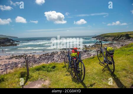 Biker ruhen sich aus, während sie Surfer beim Wellenreiten beobachten, mit den Skellig Islands im Hintergrund in St. Finan's Bay in South Kerry, Irland. Foto D Stockfoto