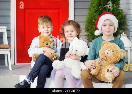 Kleine Kinder in Erwartung des neuen Jahres und Weihnachten. Drei kleine Kinder haben Spaß und spielen mit Teddybären im Innenraum mit Weihnachten de Stockfoto