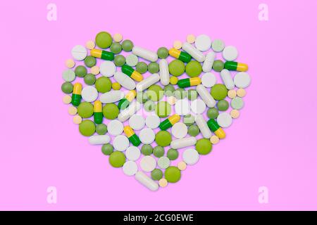 Grüne und gelbe Drogen Kapseln und Pillen auf rosa Hintergrund. Bunte Pillen in der Form des Herzens gelegt. Stockfoto