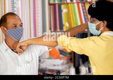 Ladenbesitzer begrüßt den Kunden mit Ellenbogenstoß im Tuchladen - Konzept der Menschen vermeiden Handschlag an Geschäftsstellen zu Stoppen Sie die Verbreitung von Coronavirus Stockfoto