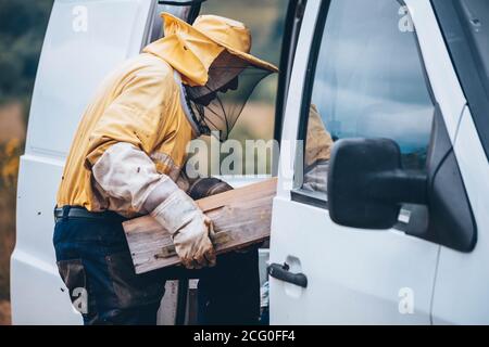 Portrait eines Imkers in Schutzkleidung, der den Bienenstock zum Auto trägt. Bienenzuchtkonzept Stockfoto