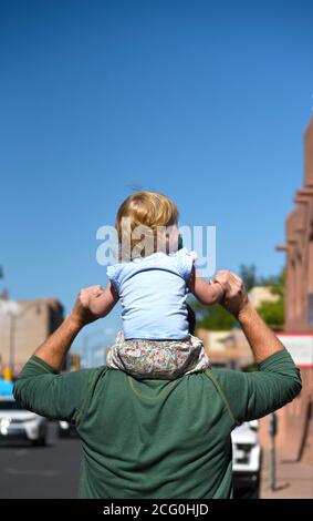 Ein Mann trägt seine junge Tochter auf seinen Schultern, während sie einen Bürgersteig in Santa Fe, New Mexico, hinuntergehen. Stockfoto