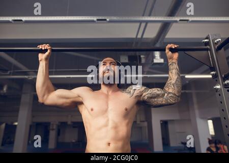 Kräftig tätowiert in weiß unbeschriftete Tank T-Shirt männlichen Athleten zeigt Calisthenic Moves close up Pullup Hold bei Medium Move On Zugstange Stockfoto