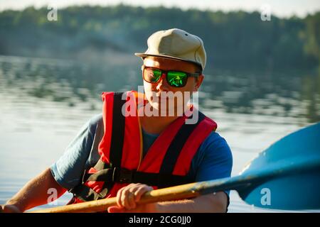 Ein Kerl in einer Schwimmweste hält ein Paddel in Seine Hände beim Schlafen auf einem Kanu Stockfoto