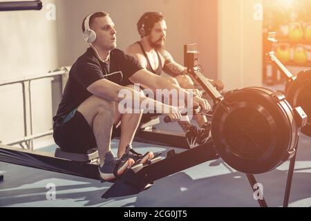 Mittelteil der Menschen, die auf dem Rudergerät im Fitnessstudio trainieren Stockfoto