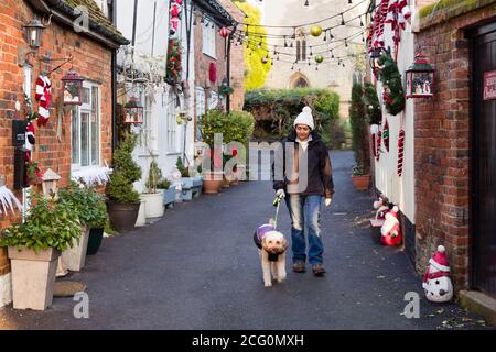 Britisch asiatisch indisch Frau Wanderhund an Weihnachten in ein Hübsche britische Straßenszene mit alten Hütten Stockfoto