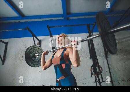 Weibchen in einem Fitnessstudio machen Kniebeugen trainieren. Junge Frau mit Langhantel mit schweren Gewichten in einem Fitnessclub trainieren. Stockfoto