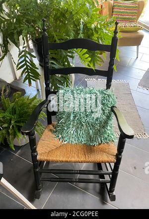 Blick auf leeren alten Holzschaukelstuhl mit grünem Kissen, Pflanzen im deutschen Wohnzimmer Stockfoto