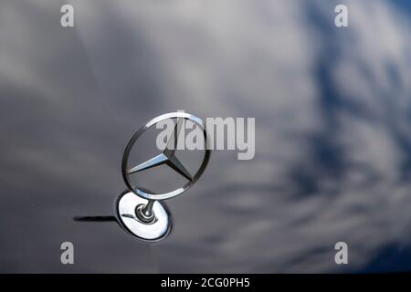 mercedes-Stern auf einer Motorhaube, in der sich Wolken spiegeln, im Freien Stockfoto