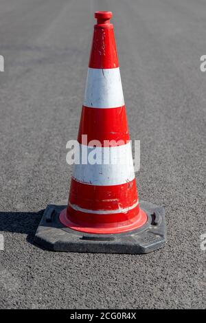 Ein einziger rot gestreifter Verkehrskegel, Pylon, auf Asphalt, im Freien Stockfoto