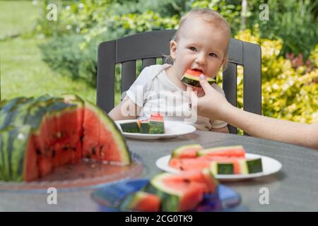 Cute Baby Junge isst Wassermelone an einem Tisch sitzen und auf der Seite schauen. Stockfoto