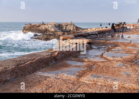 Alexandria, Ägypten - 13. Dezember 2018: Landschaft mit zerstörten Küstensteinbefestigungen. Die Leute laufen auf dem Pier Stockfoto