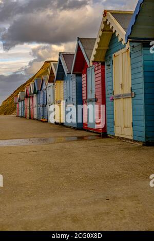 Eine Reihe von traditionellen und bunten Holzstrandhütten entlang der Promenade neben Sheringham Beach an der North Norfolk Coast. Gefangen auf einem stumpfen und o Stockfoto