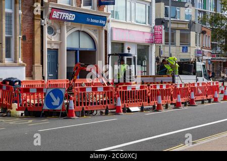 Straßendienstmitarbeiter graben eine Straße mit Verkehrsbarrieren aus Um sie herum Stockfoto