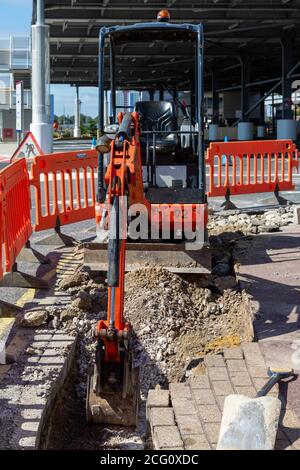 Ein kleiner Bagger gräbt den Bürgersteig während der Bodenarbeiten Stockfoto