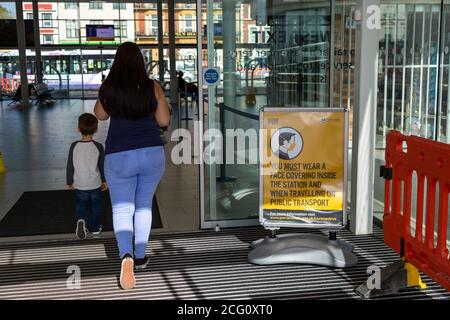Eine Mutter und ein Kind gehen an einem Schild vorbei, das das zeigt Gesichtsmasken oder Gesichtsbedeckungen müssen getragen werden Stockfoto
