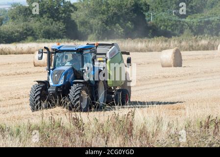 Pressen von Strohrollen in der englischen Landschaft Stockfoto