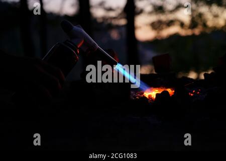 Hand hält Manul Gasbrenner in der Nähe von Brennholz in der Nacht Stockfoto