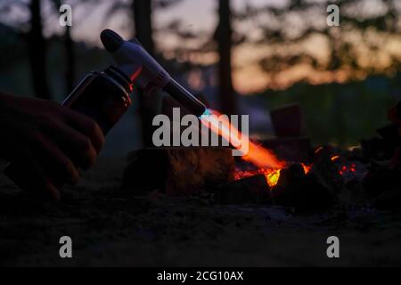 Hand hält Manul Gasbrenner in der Nähe von Brennholz in der Nacht Stockfoto