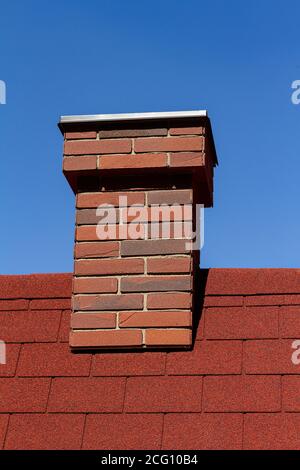 Roter Ziegelkamin auf rotem Dach mit blauem Himmel dahinter Stockfoto