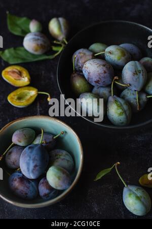 Nahaufnahme von Schüsseln mit frischen Pflaumen vor schwarzem Hintergrund. Stockfoto