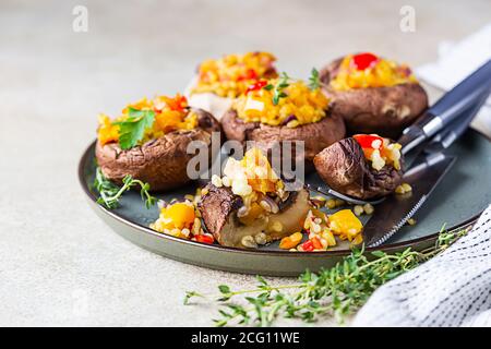 Gebackene gefüllte portobello-Pilze mit Bulgur-Pilaf und gehacktem Gemüse. Leckeres und nahrhaftes vegetarisches Gericht. Steinhintergrund, selektiver FOC Stockfoto